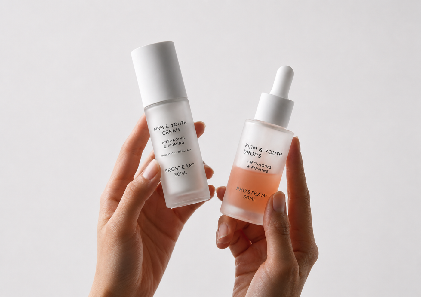 Two hands holding two skincare bottles against a light gray background. The left bottle is frosted white with a white cap, and the right bottle is frosted with a white dropper cap and contains a peach-colored liquid.