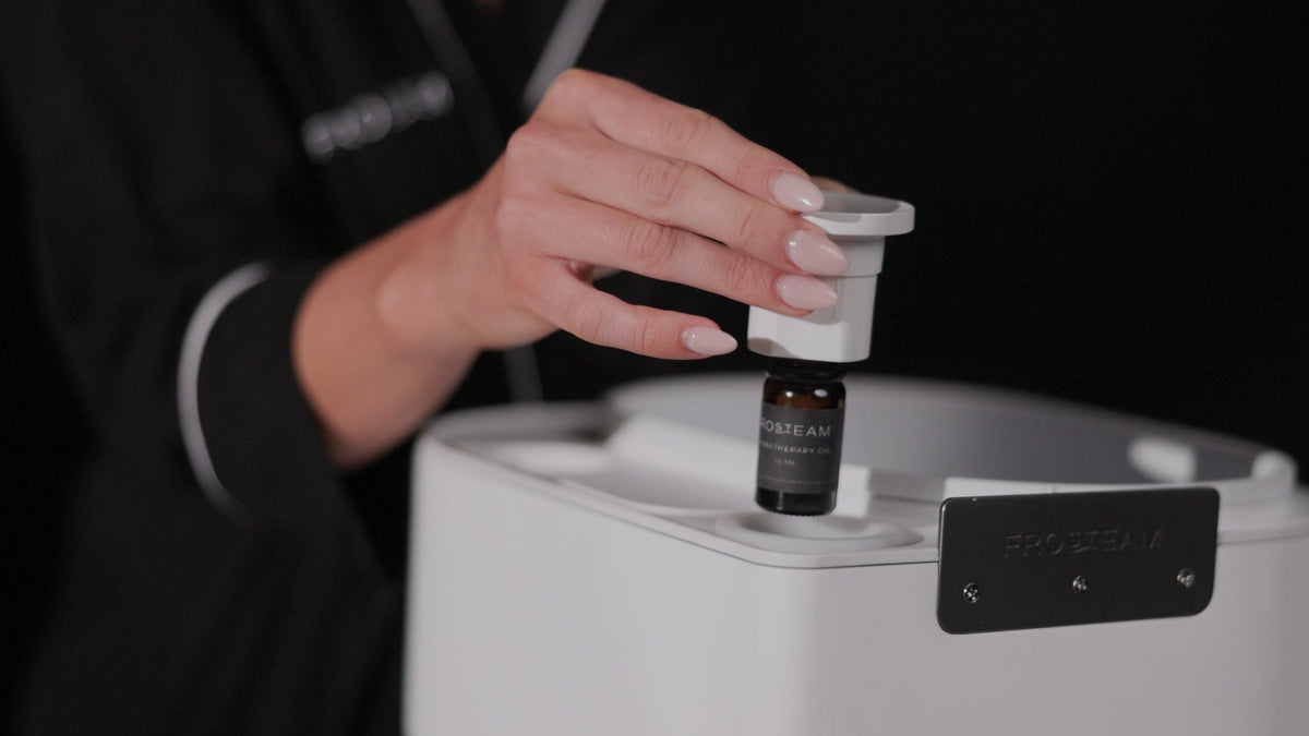 Hand placing a Frosteam essential oil bottle into the Harmony built-in diffuser