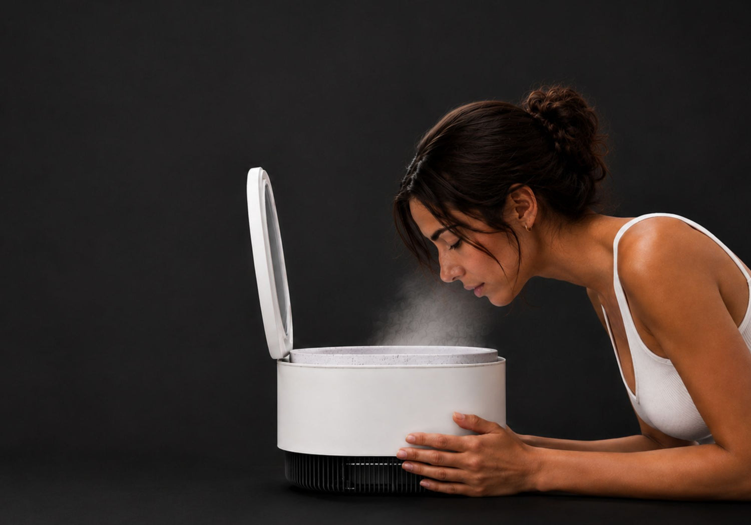 Woman leaning over the Frosteam Harmony device with warm nano-ionic steam rising during an at-home facial ritual.